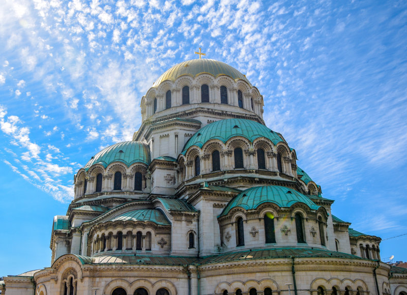 Die Alexander-Newski-Kathedrale in Sofia, Bulgarien, mit ihren markanten grünen Kuppeln und goldenen Verzierungen, gegen einen blauen Himmel mit leichten Wolken.
