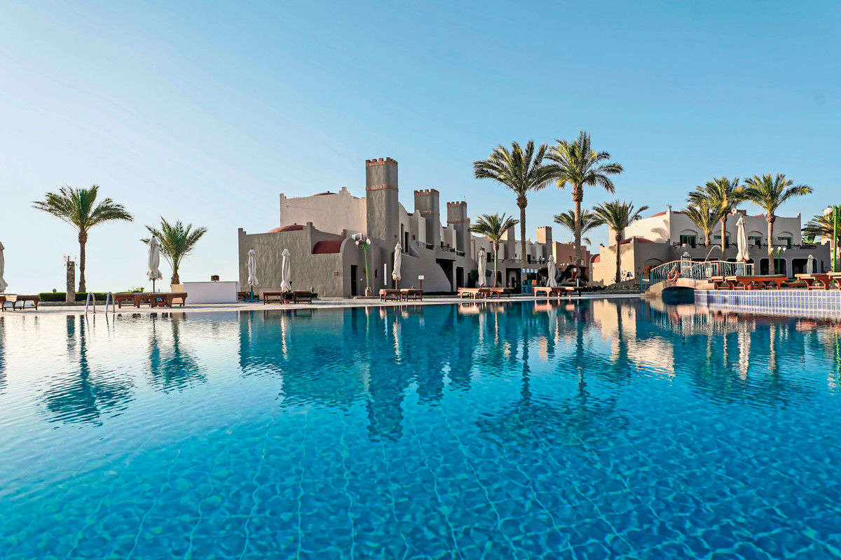 Ein Luxusresort mit traditioneller Architektur, Swimmingpool und Palmen unter einem klaren blauen Himmel.